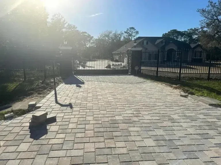 Paved driveway with metal gate and house in the background under bright sunlight