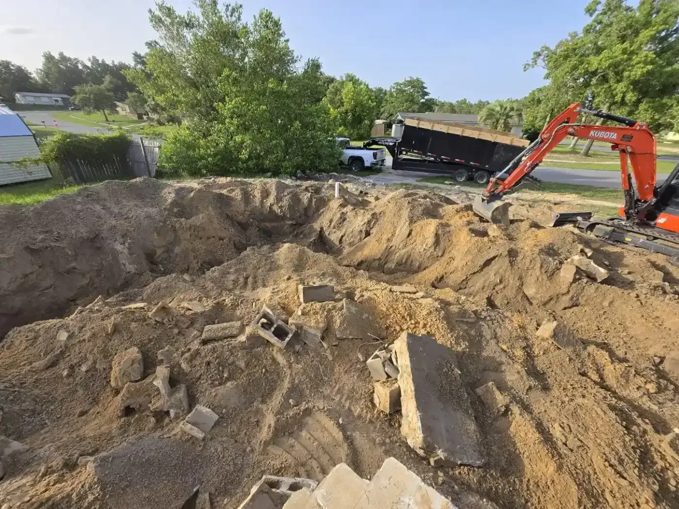 Excavator at a large muddy construction dig site under a bright sky