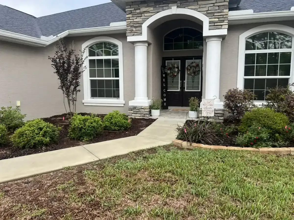 Front entrance of a house with stone arch, white columns, arched windows, and a landscaped front yard