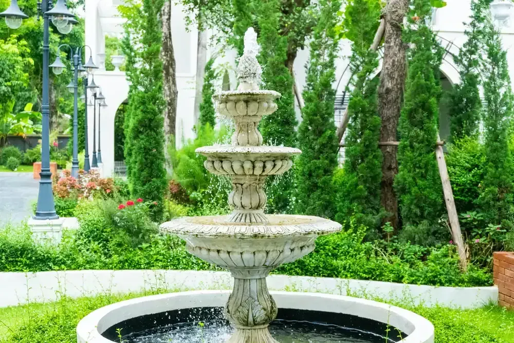 Tiered stone fountain in a lush green garden with trees and flowers