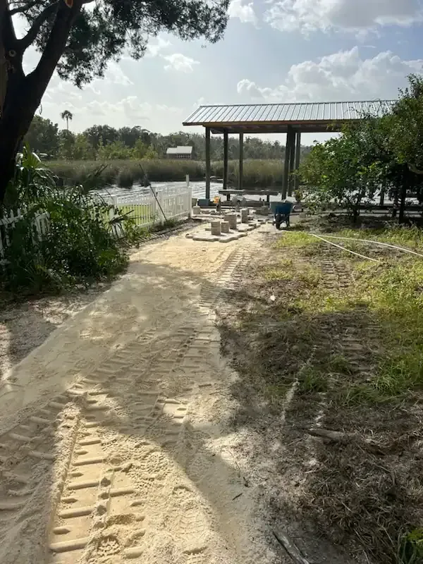 Sandy path leading to a small riverside pavilion beside calm water and trees