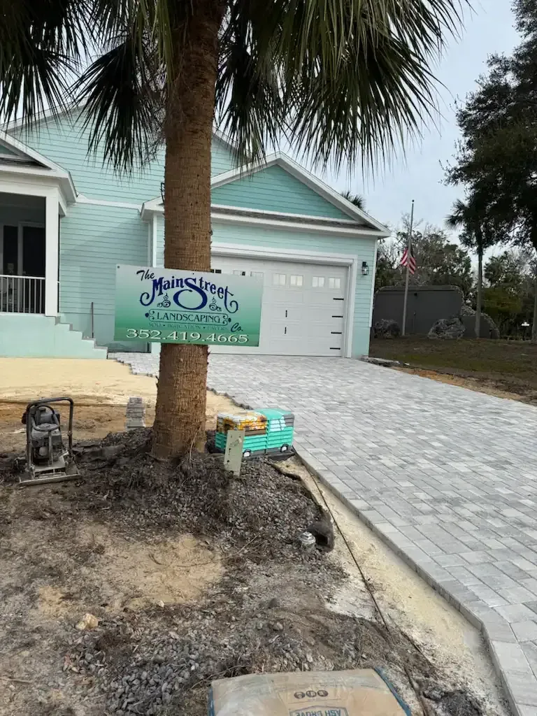 Sign in front of a teal house with a white garage and paved driveway.