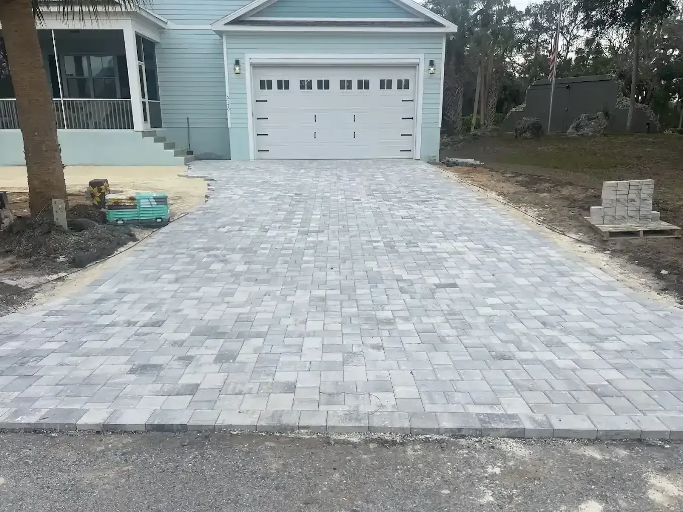Stone paver driveway leading to a white garage on a light blue house.