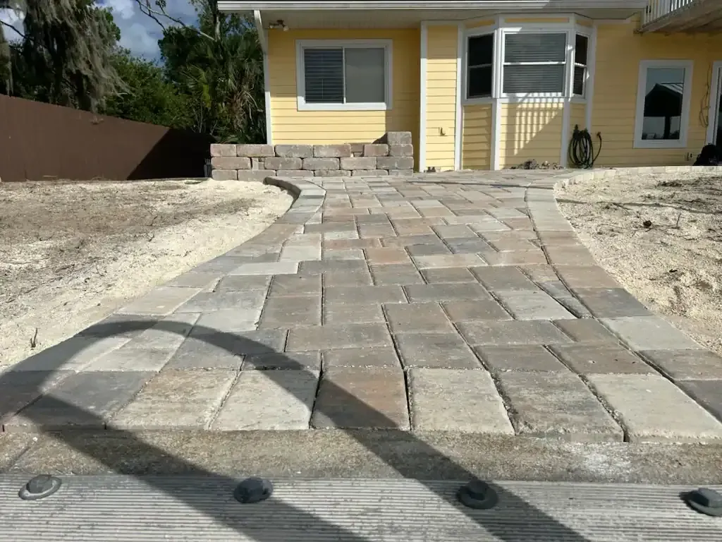 Stone walkway leading to a yellow house with a white front door and sandy landscaping