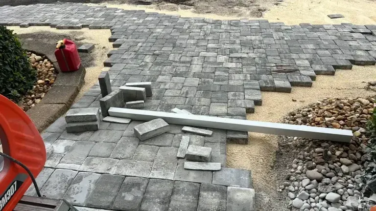 Broken gray metal pipe lying across a stone patio with scattered pavers and rocks