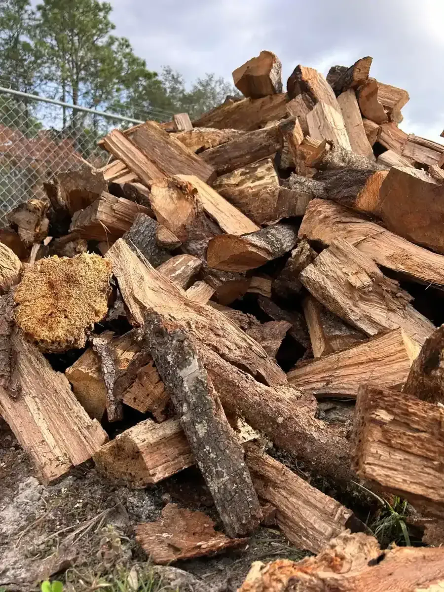 Pile of split firewood stacked outdoors beneath a blue sky.