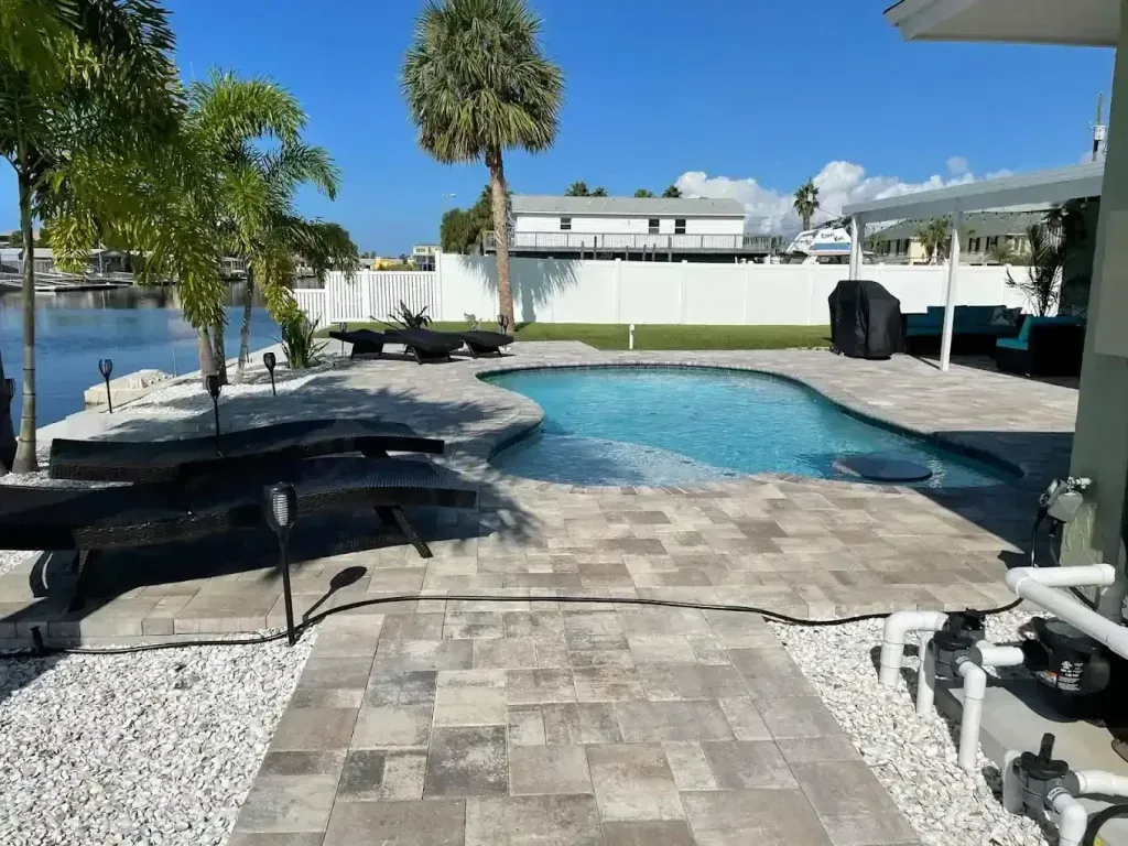 Poolside patio with lounge chairs, palm trees, and waterfront view under a sunny sky