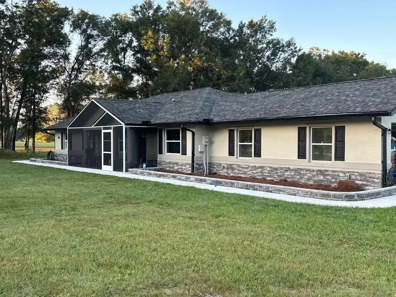 Single-story beige house with dark roof, white trim, and a wide green lawn at dusk