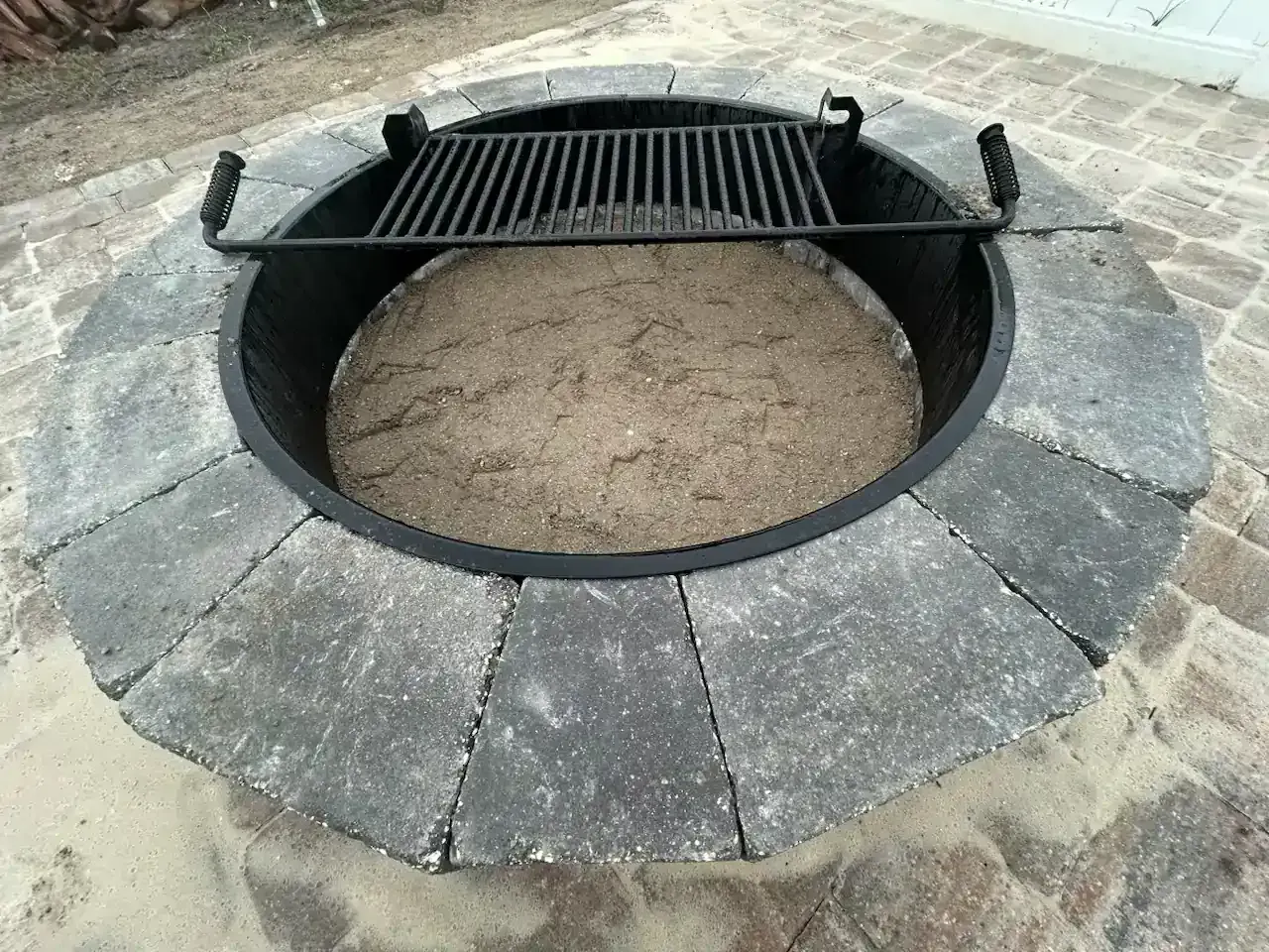 Stone fire pit with a black metal grate set into a circular brick surround