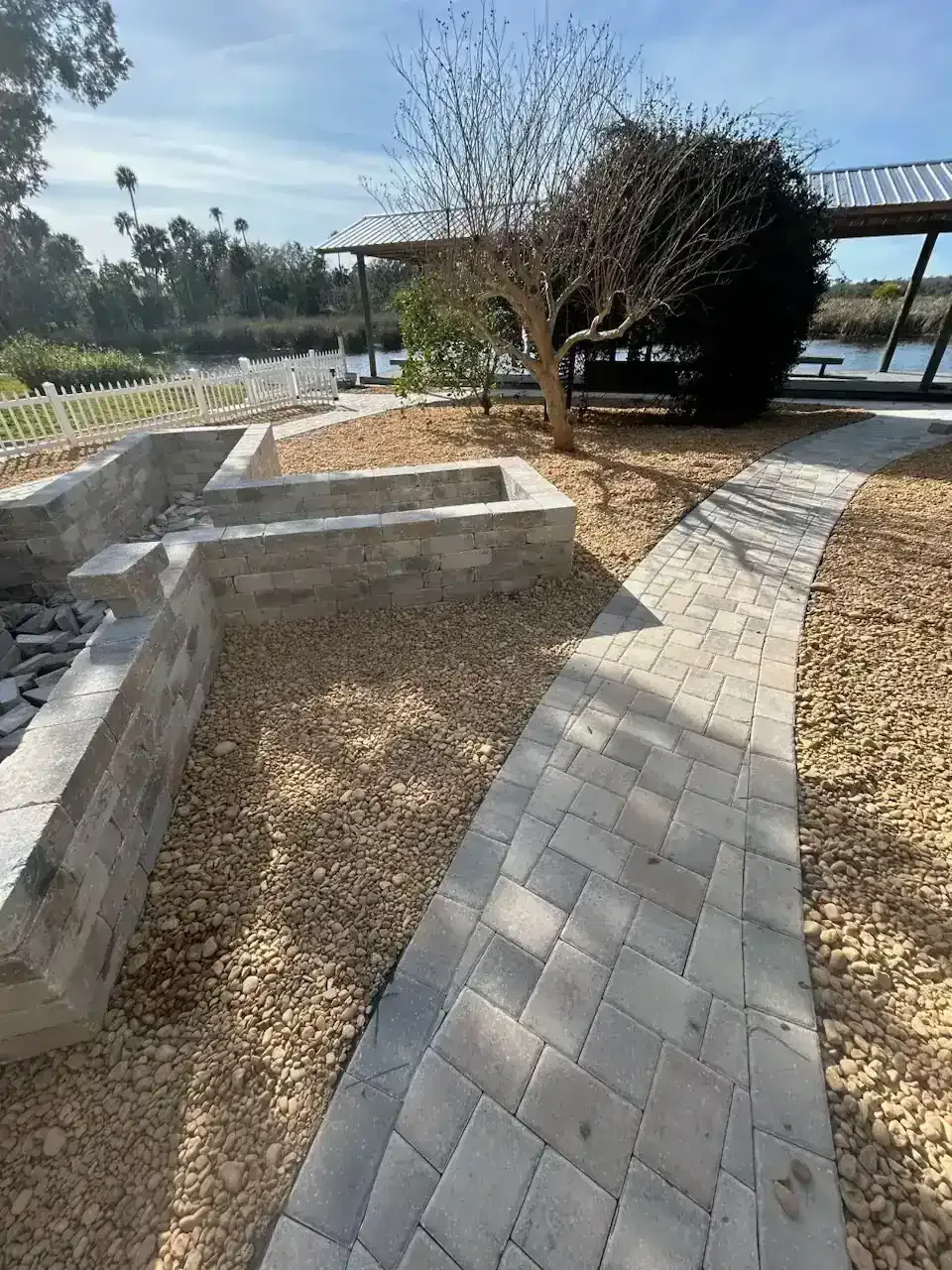 Curved stone walkway beside raised concrete planters and a tree in a landscaped outdoor park.