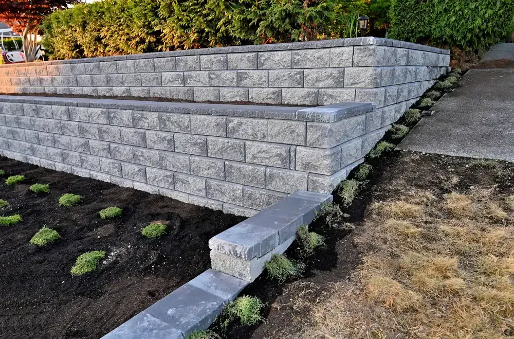 Stone retaining wall with steps in a landscaped yard, bordered by shrubs and soil beds