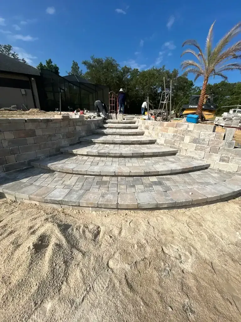Stone steps in a landscaped courtyard leading upward beside a sandy area and palm trees under a clear blue sky