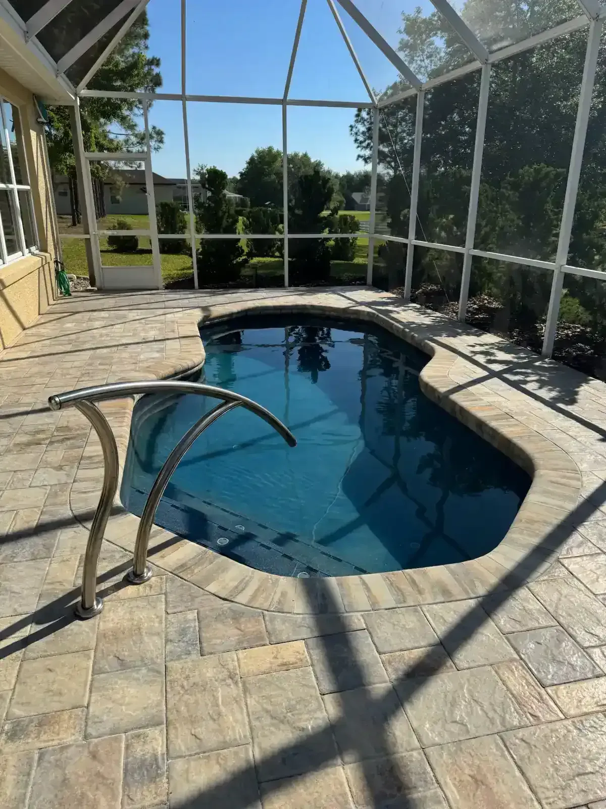 Screened-in patio with small blue pool, stone deck, and lounge chair in sunlight