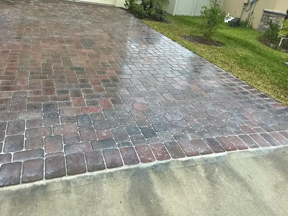 Wet red brick driveway beside a concrete edge and green lawn