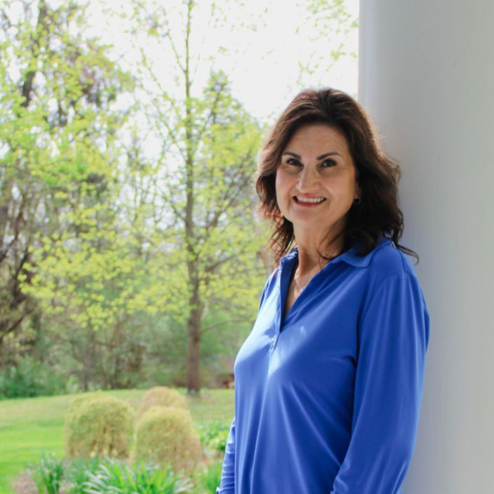Person in a red blouse and beige pants standing on a sunlit colonnade walkway