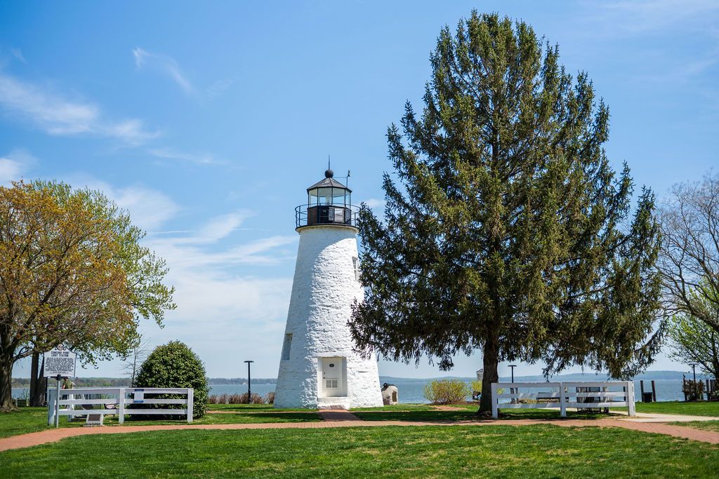 White lighthouse in a grassy park by the water under a blue sky