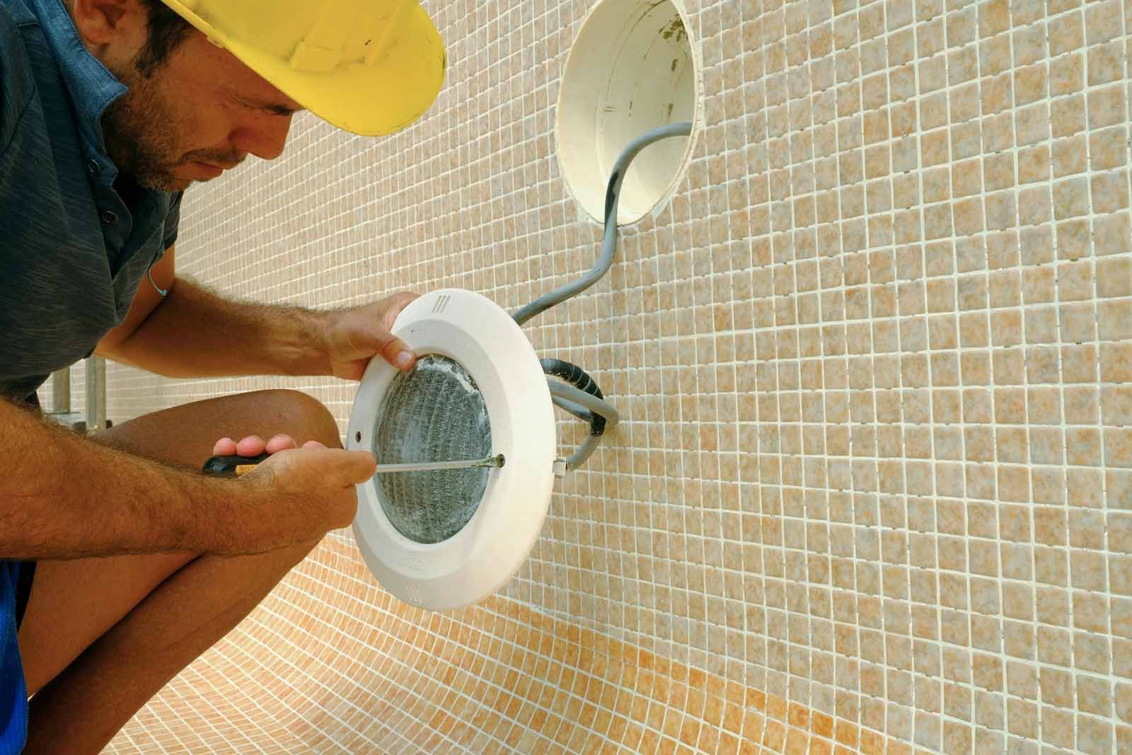A man is installing a light on a tiled wall.