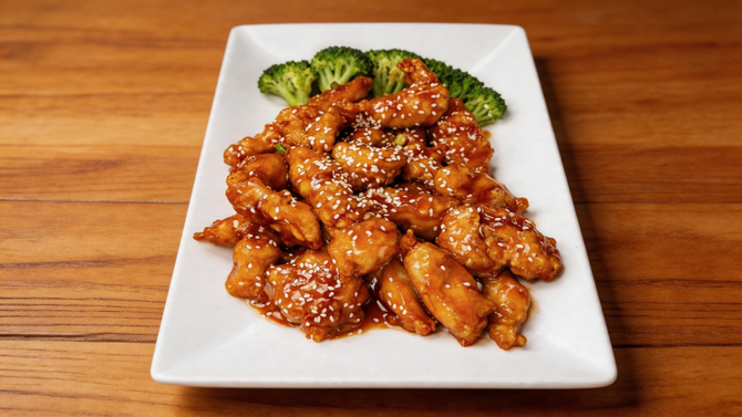 A plate of sesame chicken with green beans and steamed broccoli, served on a blue and white patterned dish on a table.