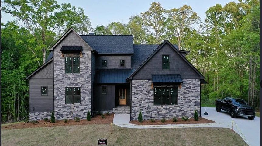 Modern two-story house with stone and dark siding, black roof, and a black truck parked in the driveway.