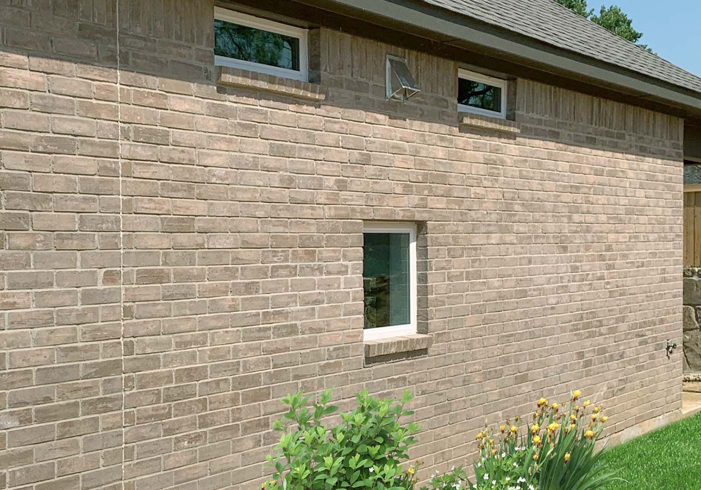 Brick exterior of a building with three windows, a satellite dish, and some landscaping.
