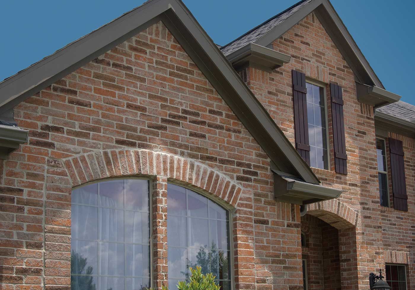 Brick house exterior with arched windows and brown shutters.