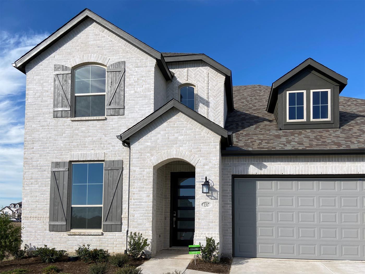 Two-story brick house with gray shutters and garage door against a blue sky.