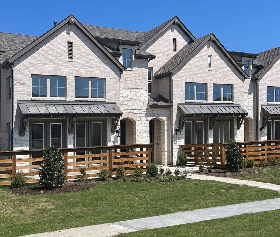 Row of brick townhouses with metal awnings, wood fence, and green lawn.