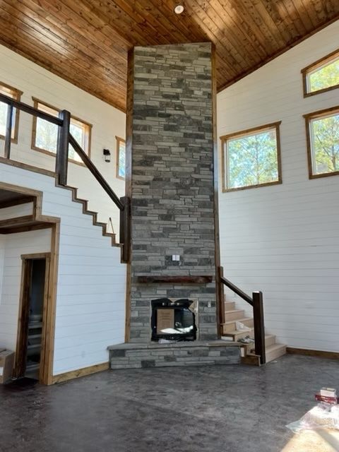 Stone fireplace in a cabin-style room with stairs, windows, and wood ceiling.