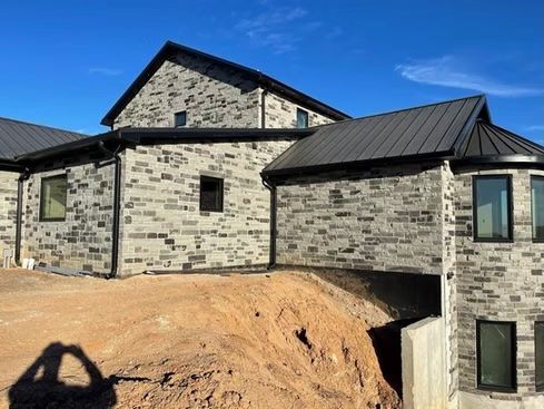 Modern stone house with black roof, gutters, and windows against a blue sky.