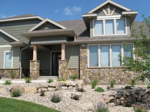 Green and stone-faced house with a landscaped yard and a blue sky.