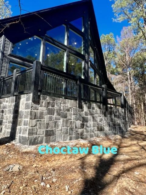 Black cabin with stone foundation and large windows against a blue sky.