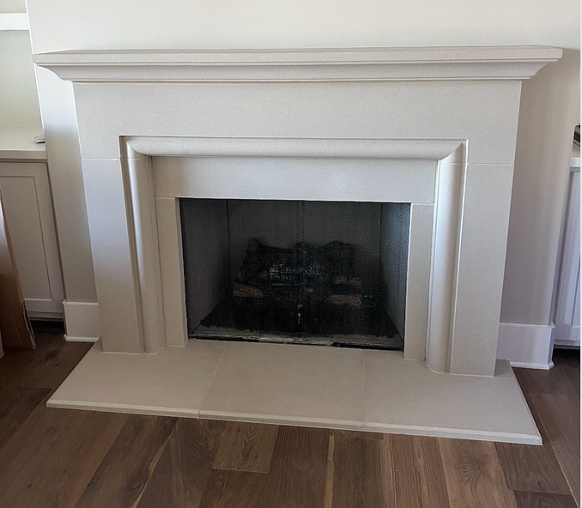 Light gray fireplace with dark interior against a wood floor.