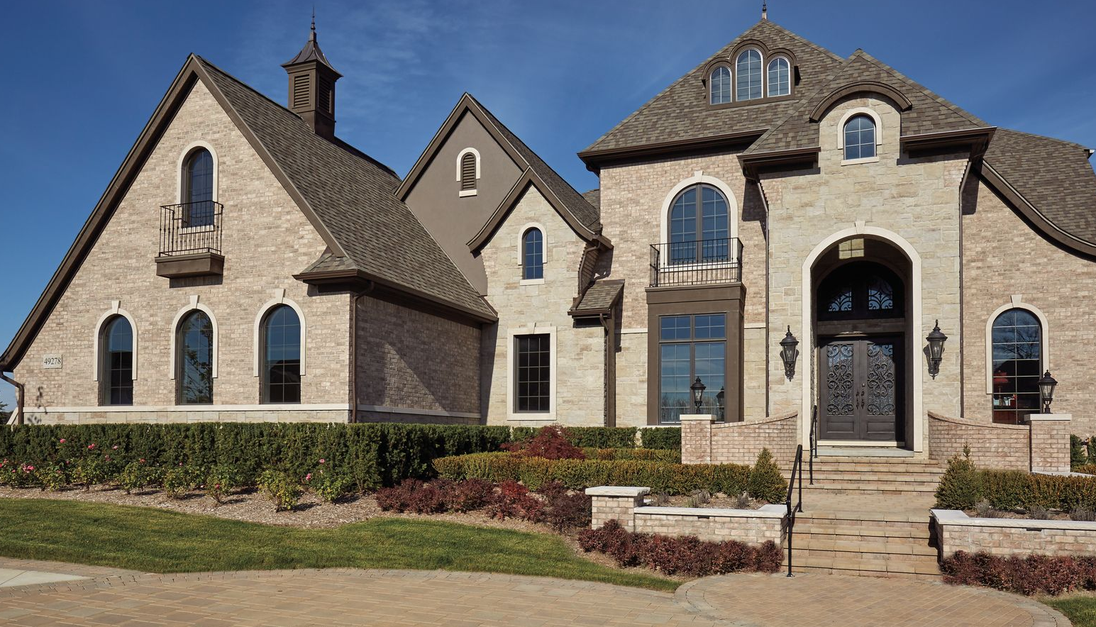 Elegant brick house with multiple gables and arched windows, set against a bright blue sky.