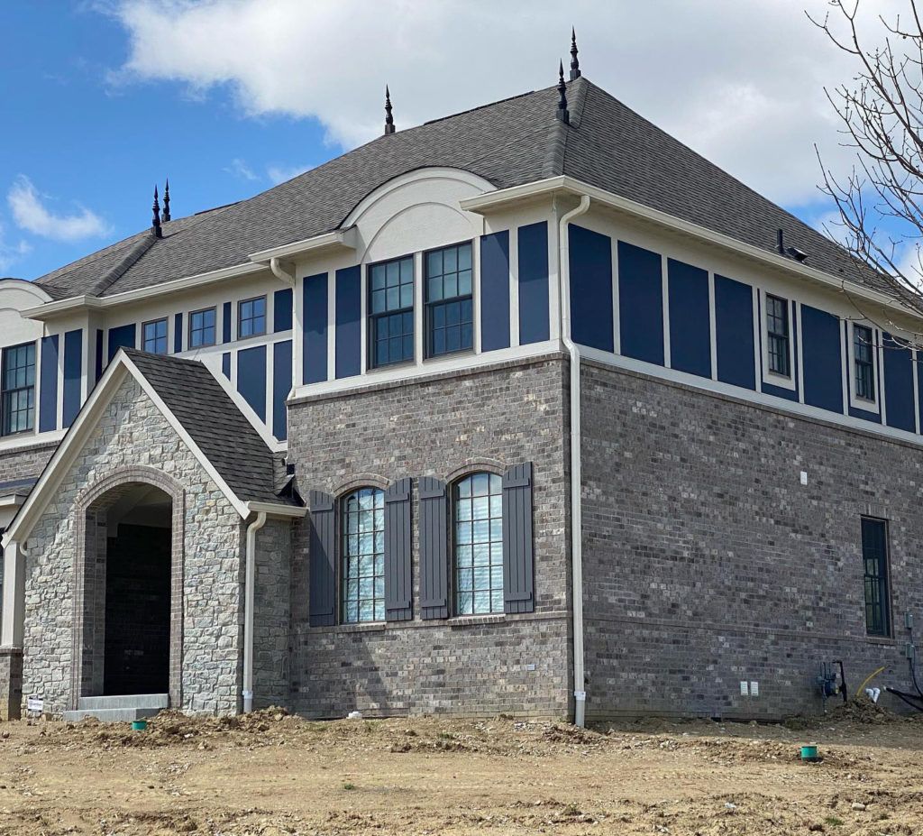 New brick home with blue accents, shutters, and roof under a blue sky.