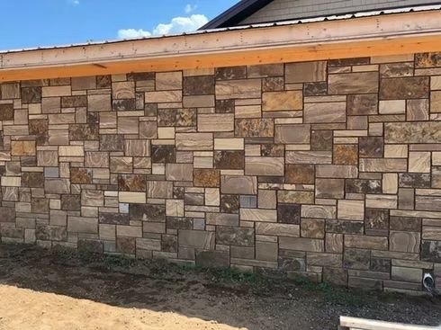 Stone veneer wall with varying shades of brown and beige, beneath a wooden eave.