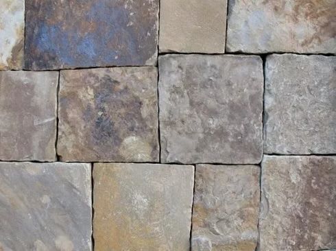 Close-up of a wall made of rectangular, rough-hewn, tan and brown stones with visible grout.