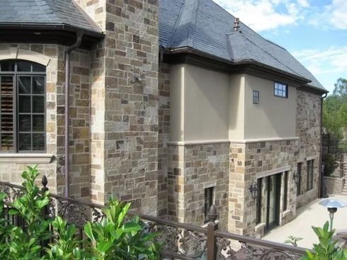 Stone and stucco house exterior with dark roof and windows.