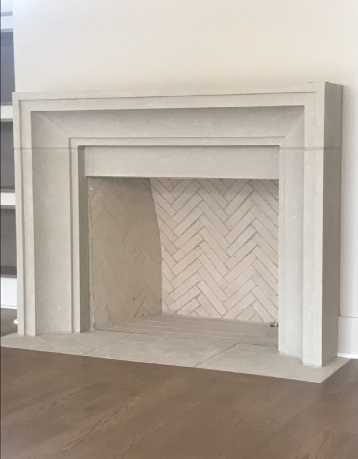 White stone fireplace with herringbone brick interior, set against a white wall and wood floor.