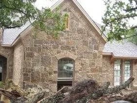 Stone house with arched window, small window in gable. Branches in foreground.