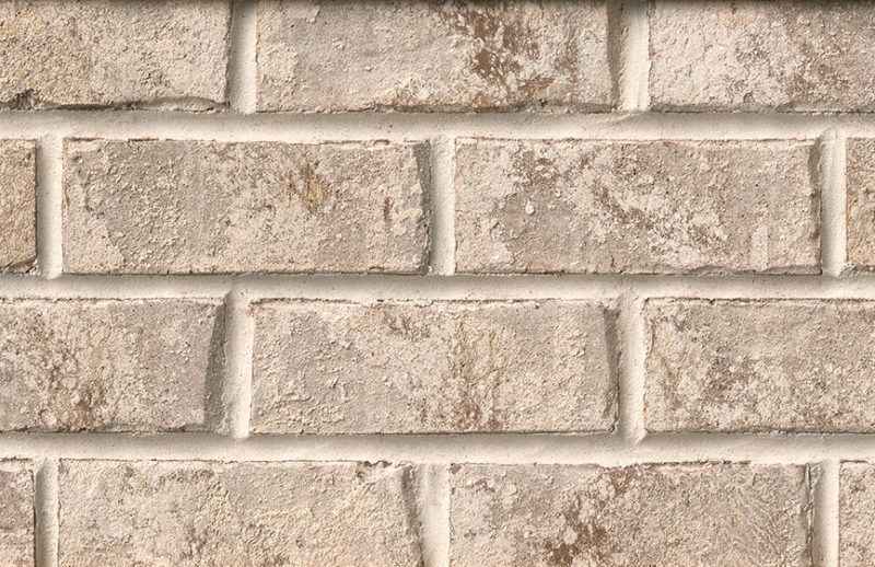 Close-up of a weathered beige brick wall with light gray mortar.