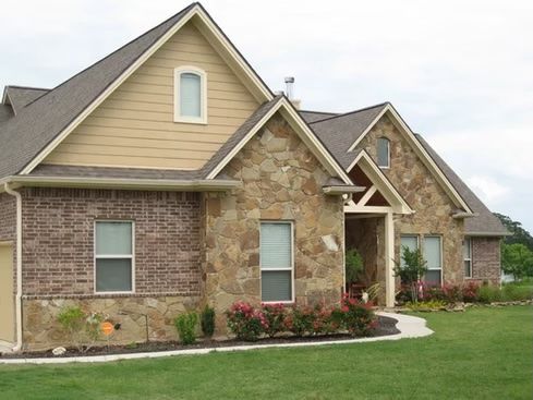 House with brick and stone exterior, tan siding, green lawn.