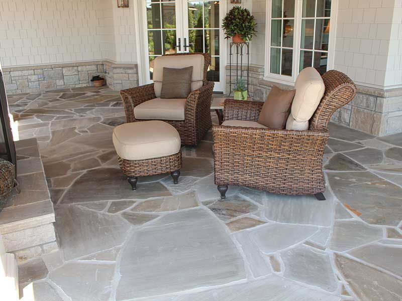 Wicker outdoor furniture on a stone patio with a fireplace and white French doors.