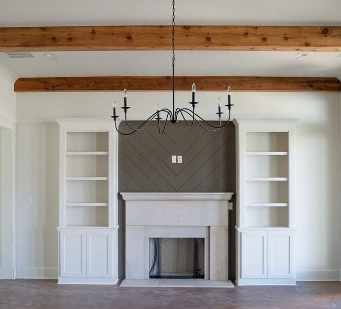 Living room with white built-in bookshelves flanking a stone fireplace, dark chandelier, and wood beams.