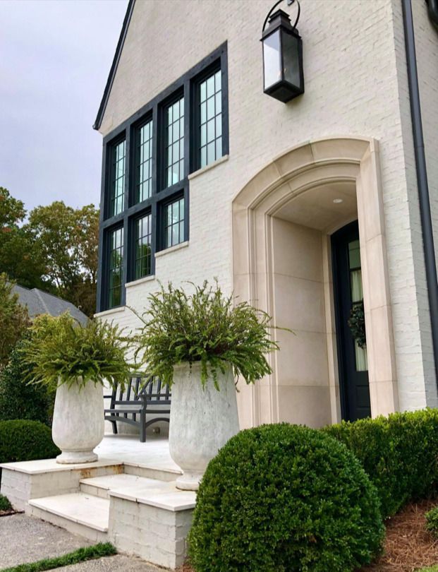 White brick house with black trim, arched entry, and decorative planters.