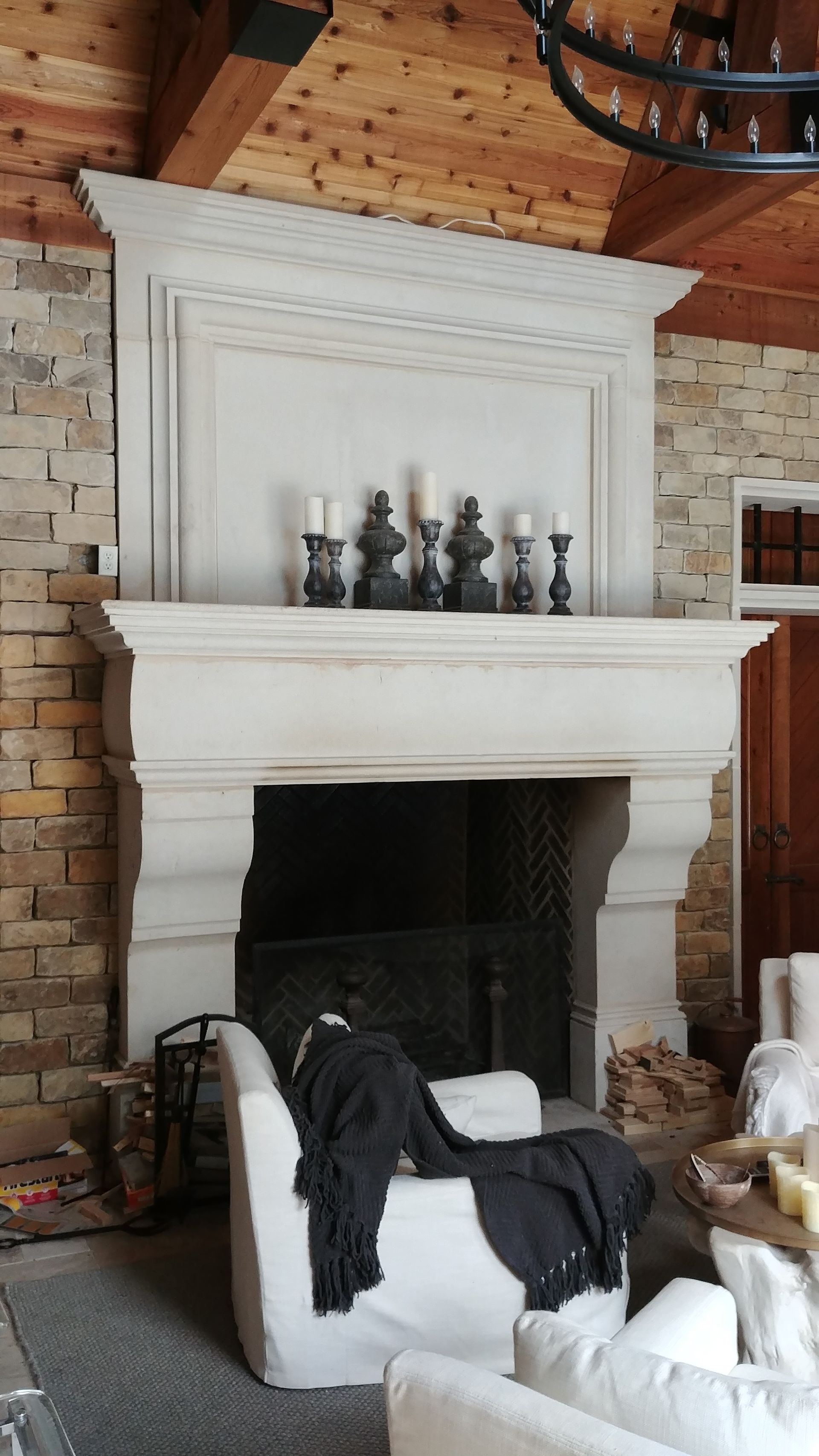 Stone fireplace with candles, a white armchair, and exposed brick wall.
