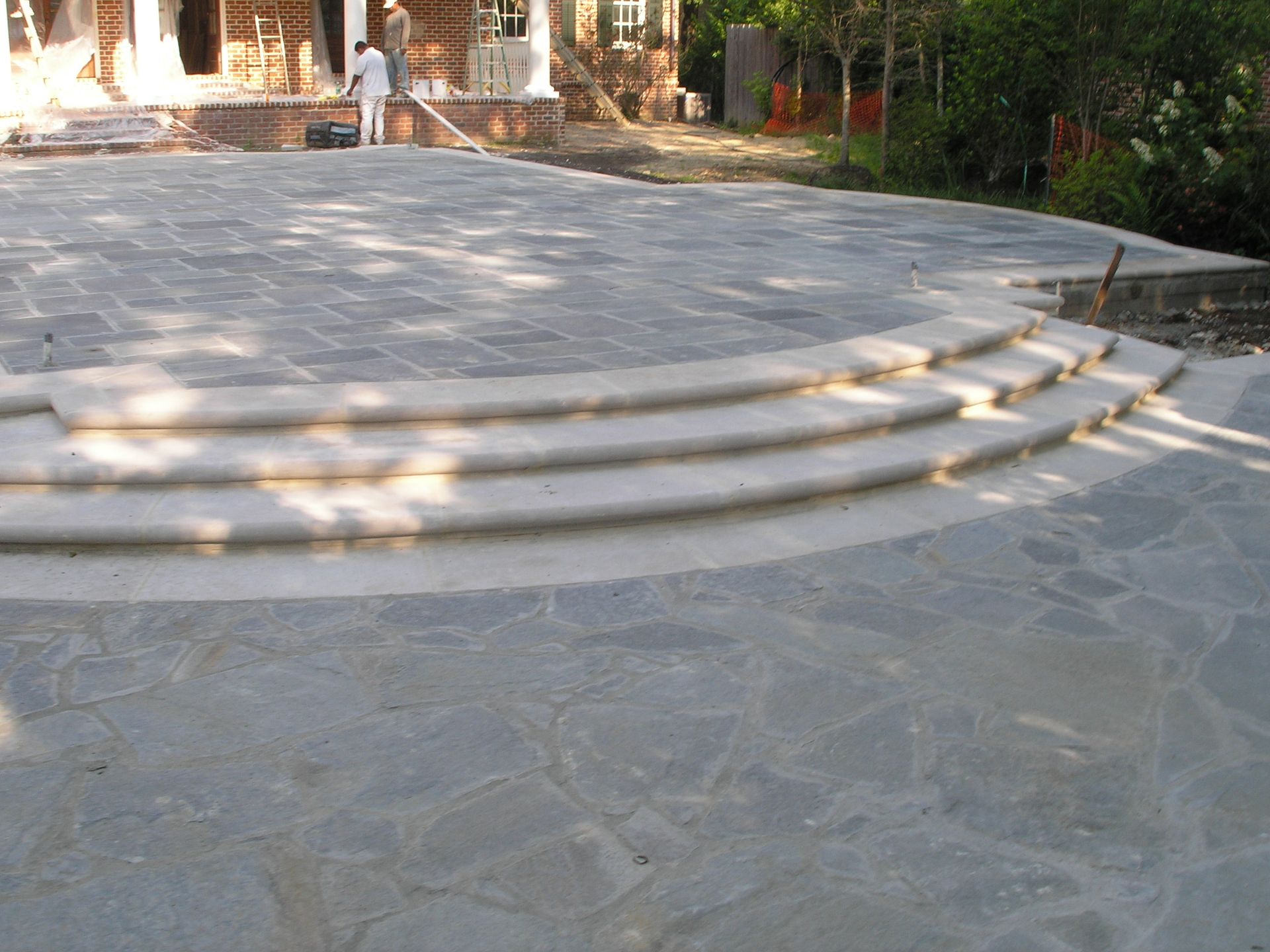Stone patio with curved steps, leading to a house under construction.