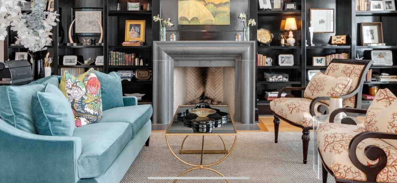 Living room with blue sofa, patterned chairs, fireplace, and bookshelves.