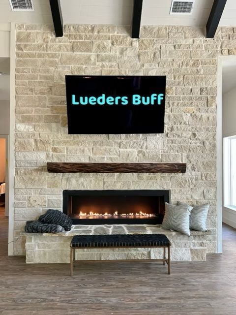 Fireplace with stone facade, TV above, wooden mantel, and bench.