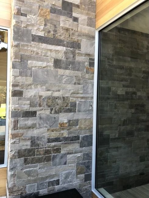 Stone-tiled exterior wall next to a large, reflective window with white framing.