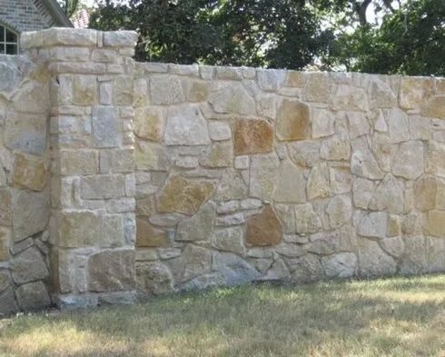 Stone wall with a pillar in a grassy area, neutral color.